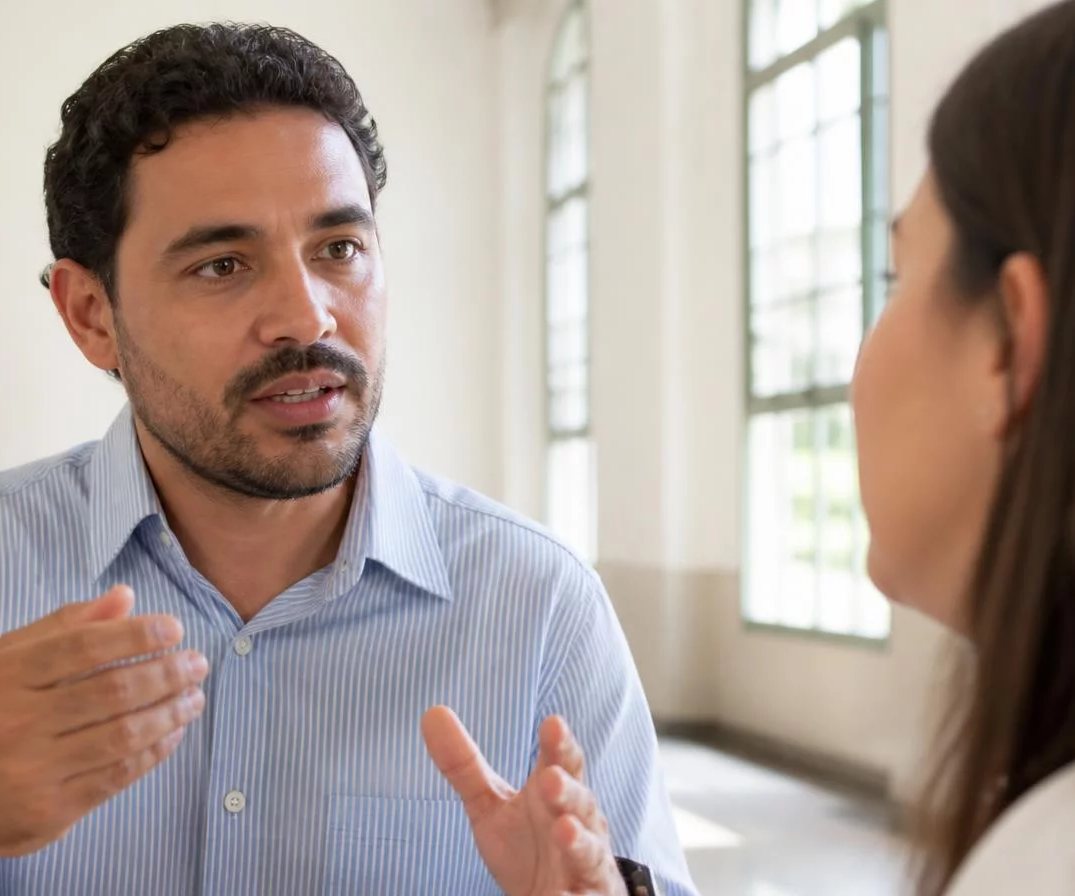 Participante com o braço no alto pedindo a vez, diante de folhas rabiscadas espalhadas pela mesa